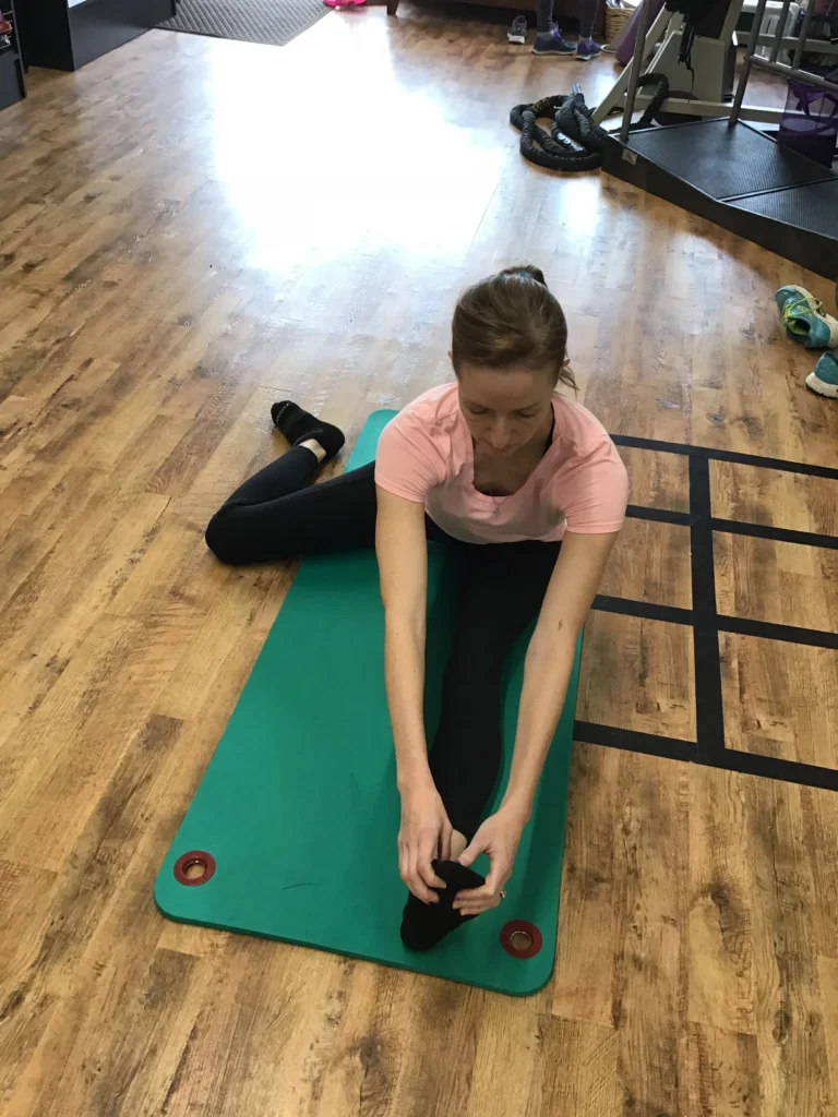 Woman sitting with left leg out and reaching for her foot