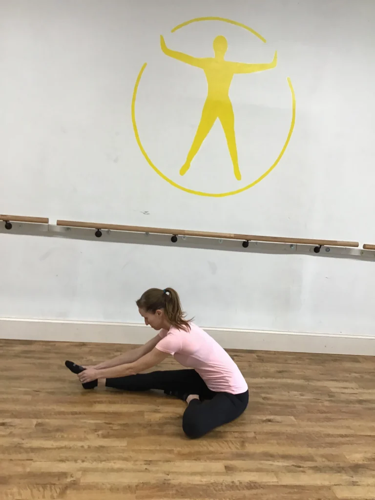 women sitting and stretching right leg out reaching for her ankle
